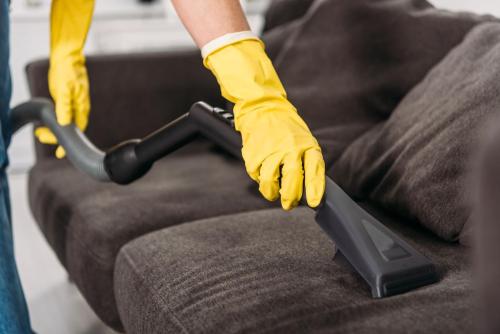 Cropped view of woman in rubber gloves cleaning sofa with vacuum